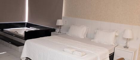 Una habitación de hotel moderna con una cama grande, un baño separado con bañera y una mesita de noche pequeña.