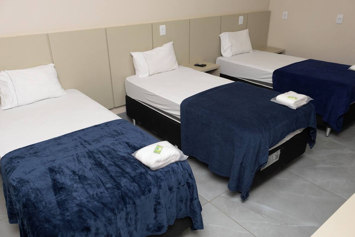 Three single beds with white linens and dark blue bedspreads in a hotel room.