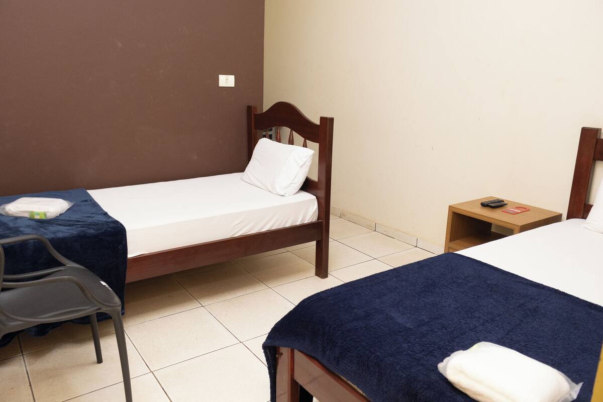 Two single beds with wooden frames, a small bedside table with a lamp, and a chair.