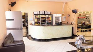 Zona de recepción de un hotel con un mostrador de mármol, un refrigerador, una cafetera y un televisor.