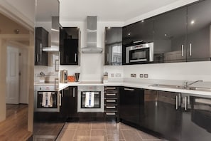 A modern kitchen with stainless steel appliances, black cabinets, and a tiled backsplash. - Elegant Soho 2-bed, bright Victorian apartment with lift, walk to Covent Garden (London)