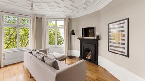 Ein Zimmer mit einer Couch, einem Kamin und großen Fenstern mit Blick auf Bäume.
