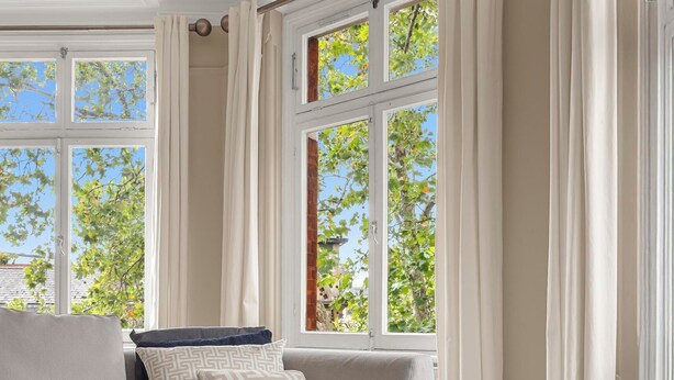 Ein modernes Wohnzimmer mit einem Ecksofa, einem gemusterten Zierkissen und Blick auf Bäume durch große Fenster.