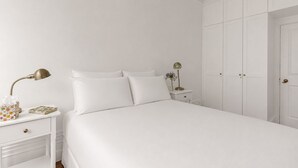 Ein helles Schlafzimmer mit Bett, Nachttischen, einer Lampe und einem Kleiderschrank.
