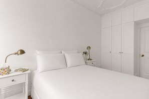A white bedroom with a bed, bedside tables, a lamp, and a wardrobe. - Elegant Soho 2-bed, bright Victorian apartment with lift, walk to Covent Garden (London)