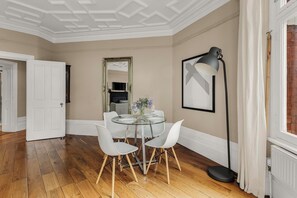 A dining area with a glass table, white chairs, a mirror, and a floor lamp. - Elegant Soho 2-bed, bright Victorian apartment with lift, walk to Covent Garden (London)