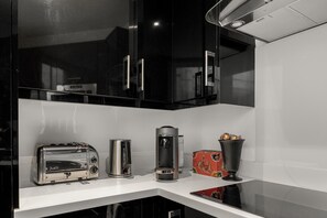 Cuina amb armaris negres, taulell blanc, torradora, cafetera i una caixa decorativa.