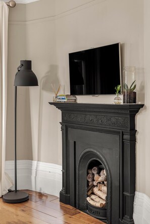 A room with a fireplace, a television mounted above it, a floor lamp, and a bookshelf with books and decorative items. - Elegant Soho 2-bed, bright Victorian apartment with lift, walk to Covent Garden (London)