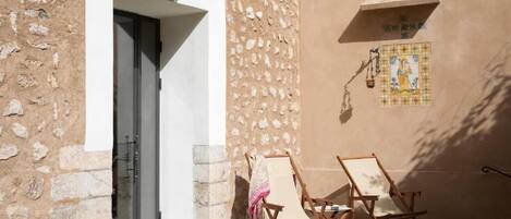 A stone building with a door, two wooden chairs, a basket, and a wall-mounted light fixture.