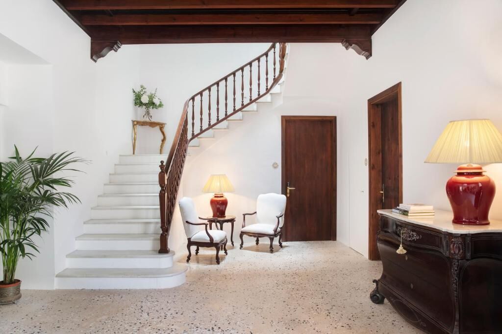 Una escalera conduce a un rellano con dos sillas y una mesa, una puerta de madera y una lámpara sobre un mueble.