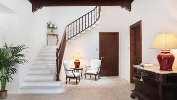 Una escalera conduce a un rellano con dos sillas y una mesa, una puerta de madera y una lámpara sobre un mueble.