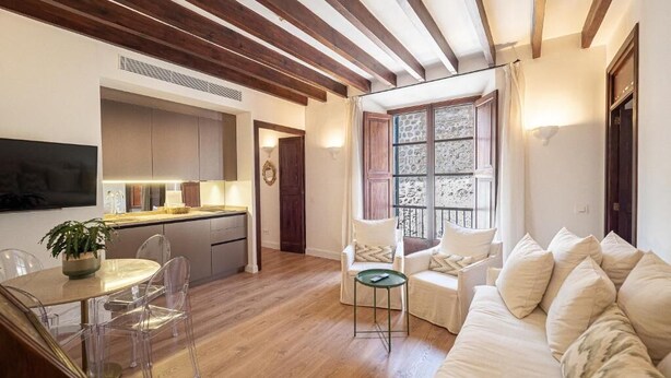 Een moderne woonkamer met houten plafond, een bank, een eettafel met stoelen en een keukenhoek.