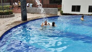 Una piscina con agua cristalina, rodeada por una terraza de madera y un edificio blanco.