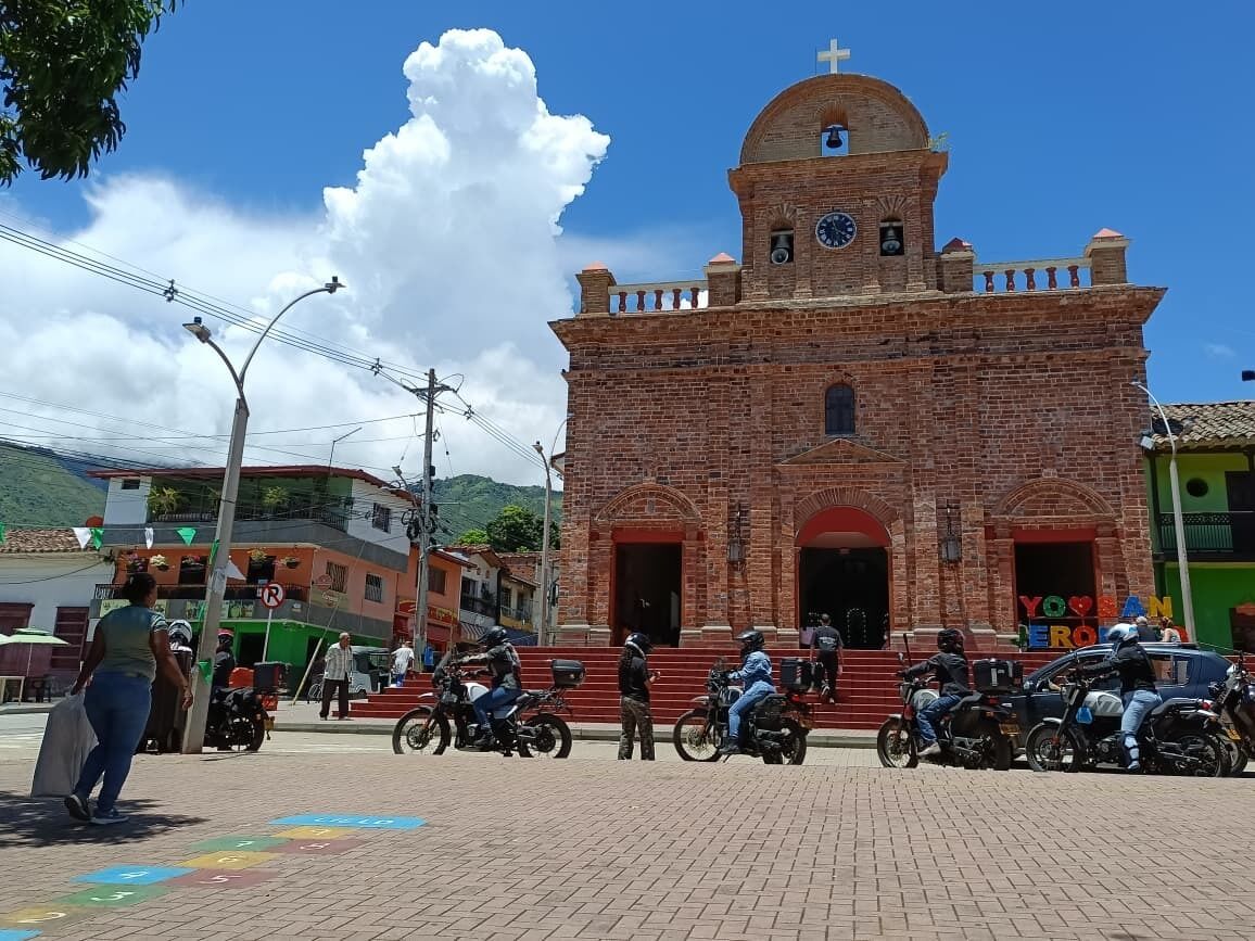 Eine Ziegelkirche mit Glockenturm und Uhr, umgeben von Motorrädern und Fußgängern.