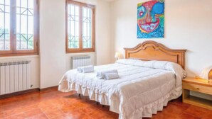 Un dormitorio con una cama grande, un radiador, una ventana y un cuadro en la pared.