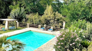 Una piscina rodeada por una valla de madera, con baldosas de piedra y una pérgola.