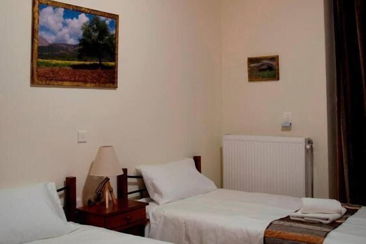 A room with two beds, a wooden ceiling, a painting on the wall, and a radiator.