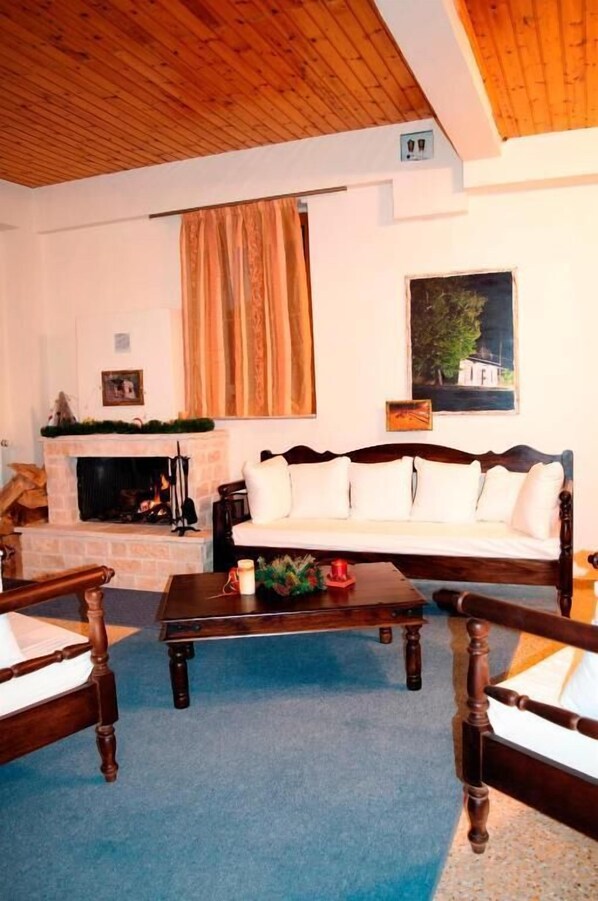 A living room with a fireplace, a sofa, a coffee table, and wooden chairs. - Xenon Achladokampos (Argos-Mykines)