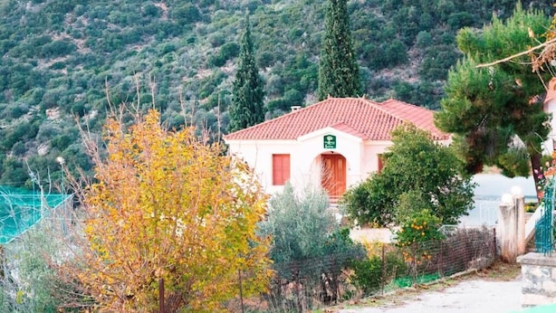 A building with a red-tiled roof, surrounded by trees and a mountainous backdrop. - Xenon Achladokampos (Argos-Mykines)