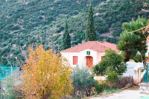 A building with a red-tiled roof, surrounded by trees and a mountainous backdrop. - Xenon Achladokampos (Argos-Mykines)