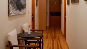 A hallway with wooden flooring, a round table with chairs, and a painting on the wall. - Xenon Achladokampos (Argos-Mykines)