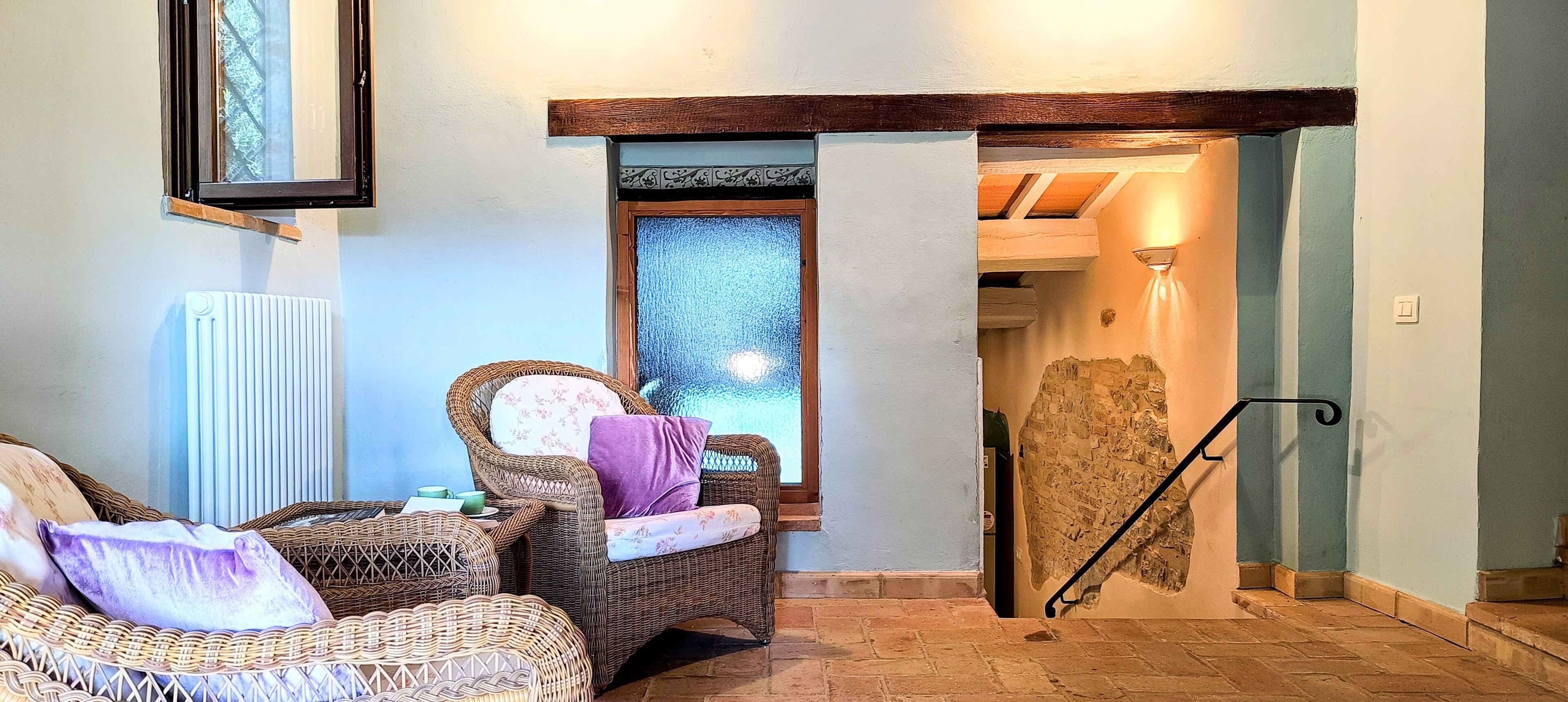 A room with wicker furniture, a radiator, a window, and a stone wall.