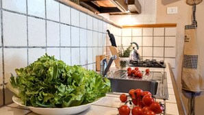 Eine Küche mit weiß gefliestem Rückspritzschutz, einer Schüssel grüner Blattsalate und einer Tomatentüte auf der Arbeitsfläche.
