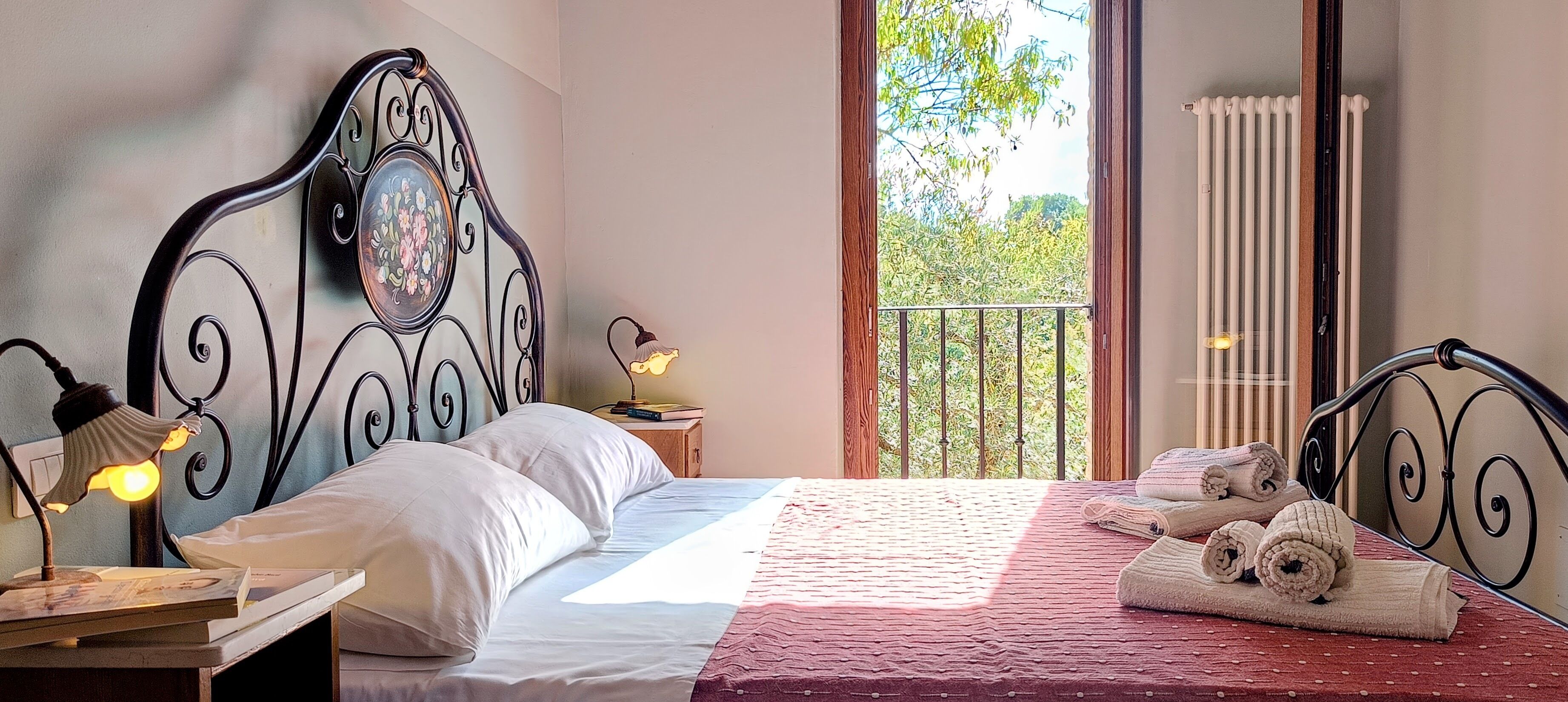Une chambre à coucher avec un lit, des oreillers, une table de chevet avec une lampe, une fenêtre donnant sur des arbres et un radiateur.
