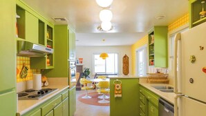 Une cuisine avec des meubles de couleur verte, une cuisinière blanche et un luminaire suspendu jaune.