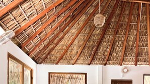 A cozy room with a thatched roof, a large window, a sofa with red cushions, and a small wooden table. - Villa Leone Privatisée (Brisas de Zicatela)