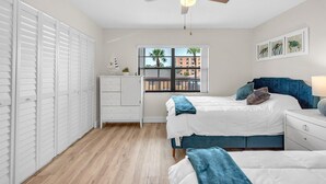 Een slaapkamer met een bed, nachtkastje, dressoir, een raam met uitzicht en een plafondventilator.