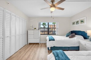 A bedroom with a bed, a nightstand, a dresser, a window with a view, and a ceiling fan. - Golden Shores #210 (Indian Shores)