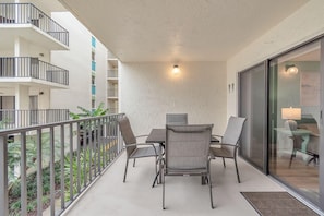 A balcony with a table and chairs, a railing, and a view of the building's interior. - Golden Shores #210 (Indian Shores)