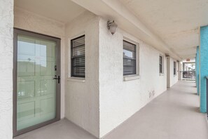 A corridor with a green door, windows with shutters, and a blue door at the end. - Golden Shores #210 (Indian Shores)