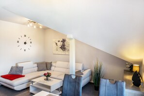 A modern living room with a white sofa, a coffee table, a clock, and a painting on the wall. - Apartment 'Above the Pub' with Wi-Fi and Air Conditioning (Michendorf)