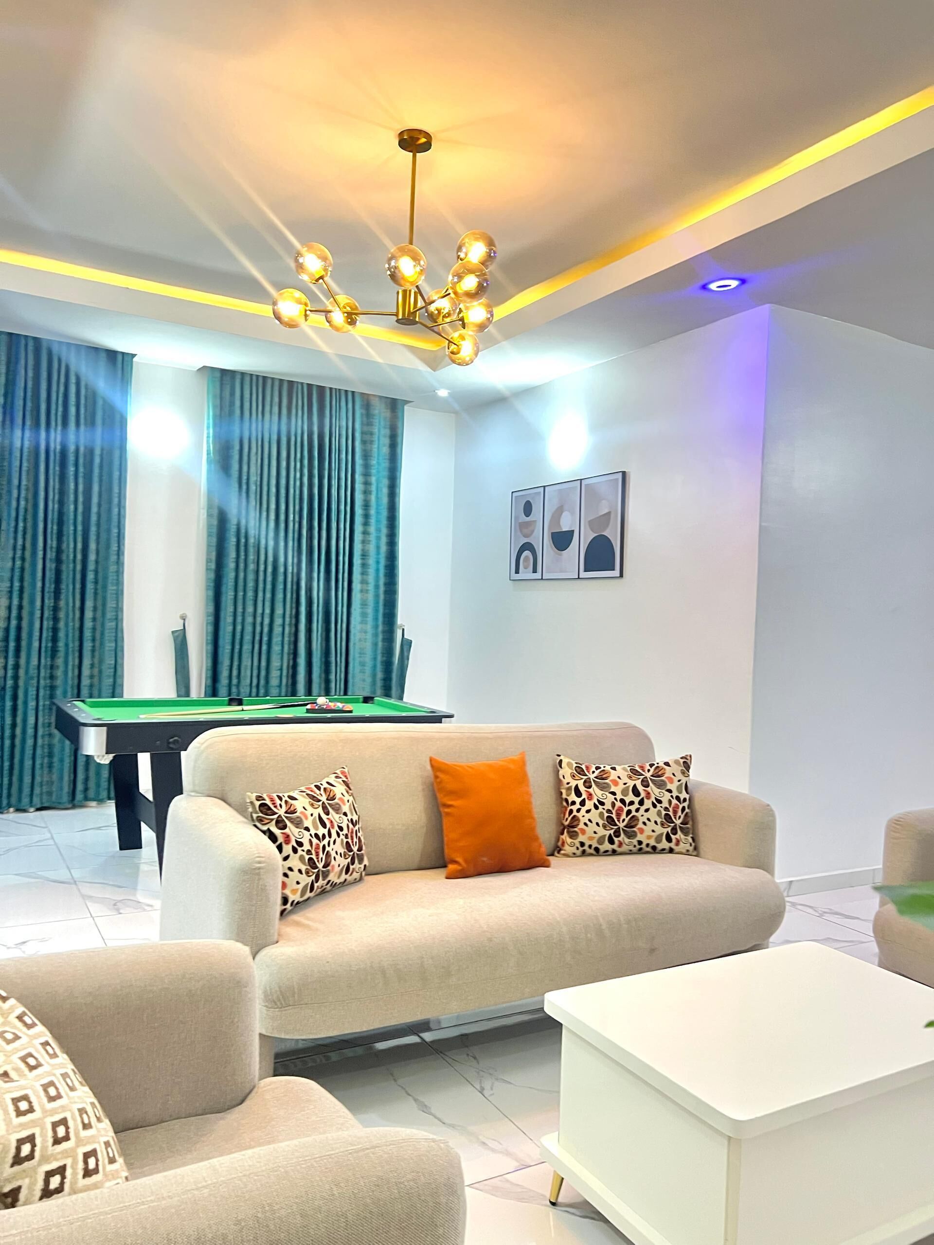 A modern living room with a pool table, a sofa with patterned cushions, and a white coffee table.
