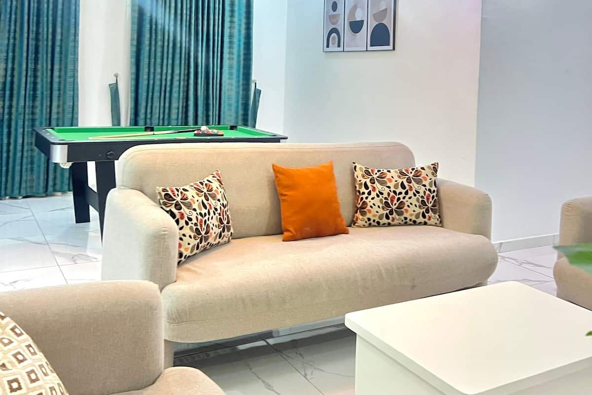 A modern living room with a pool table, a sofa with patterned cushions, a white coffee table, and a chandelier.