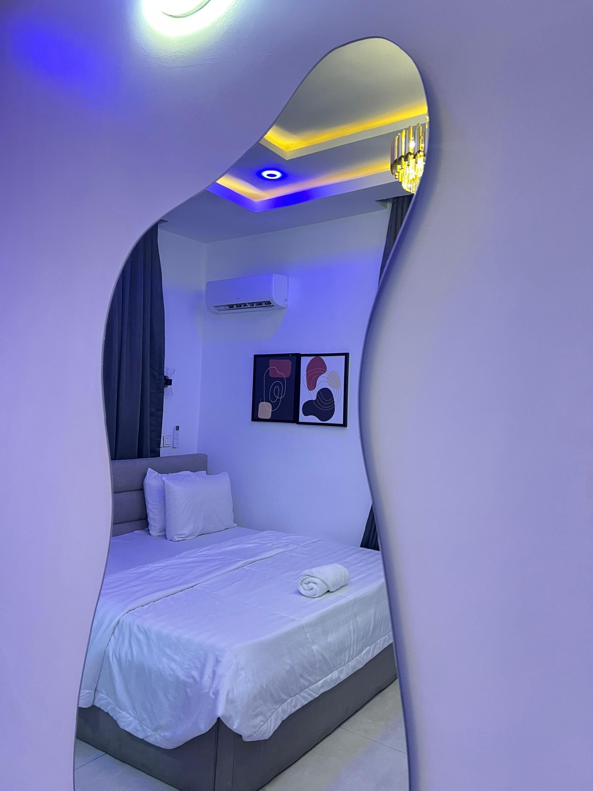 Un dormitorio moderno con un techo curvo original, una cama con ropa de cama blanca, un aire acondicionado de pared y arte abstracto.
