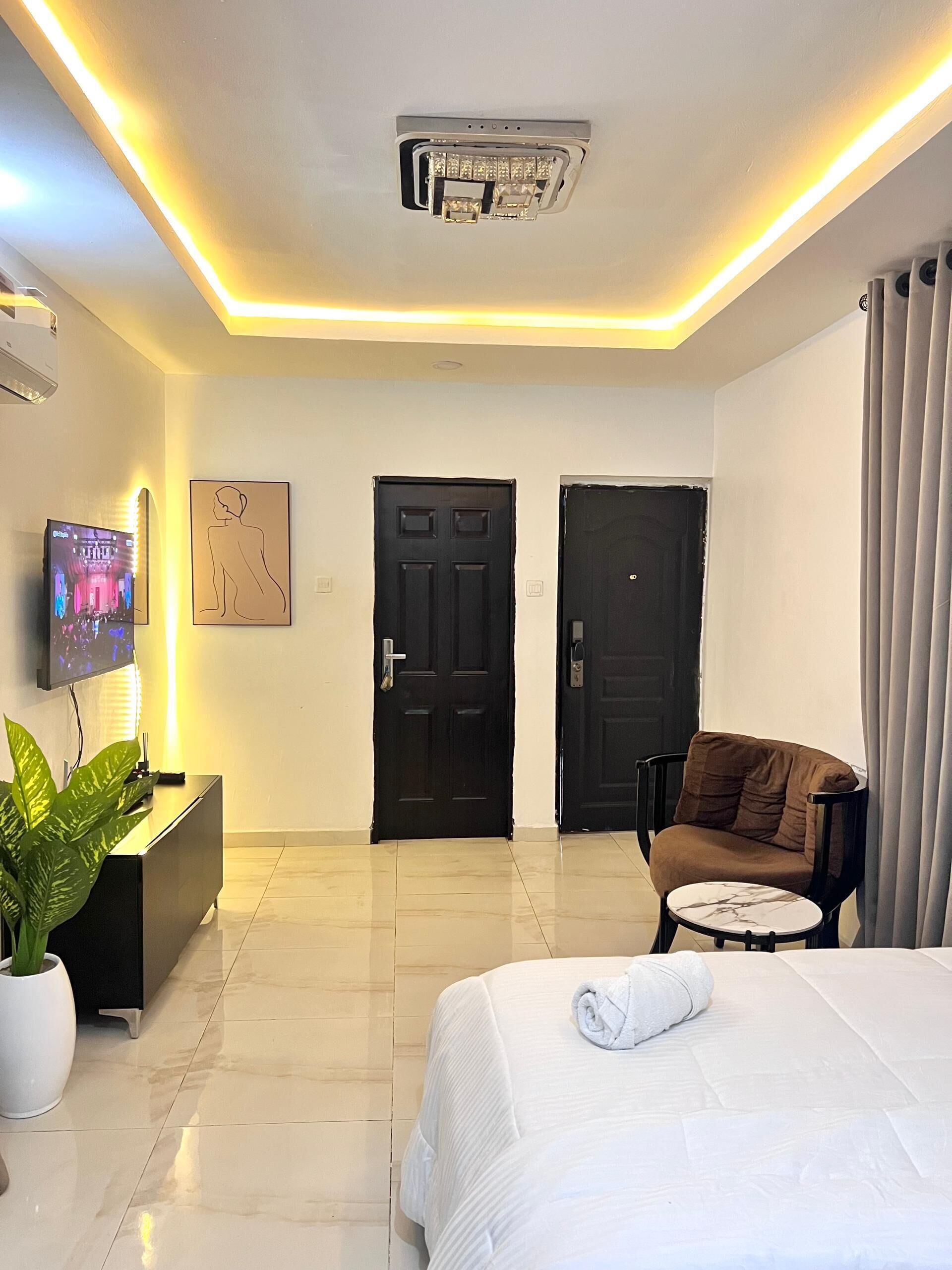 A hotel room with a bed, a TV, a desk, a chair, and two doors.