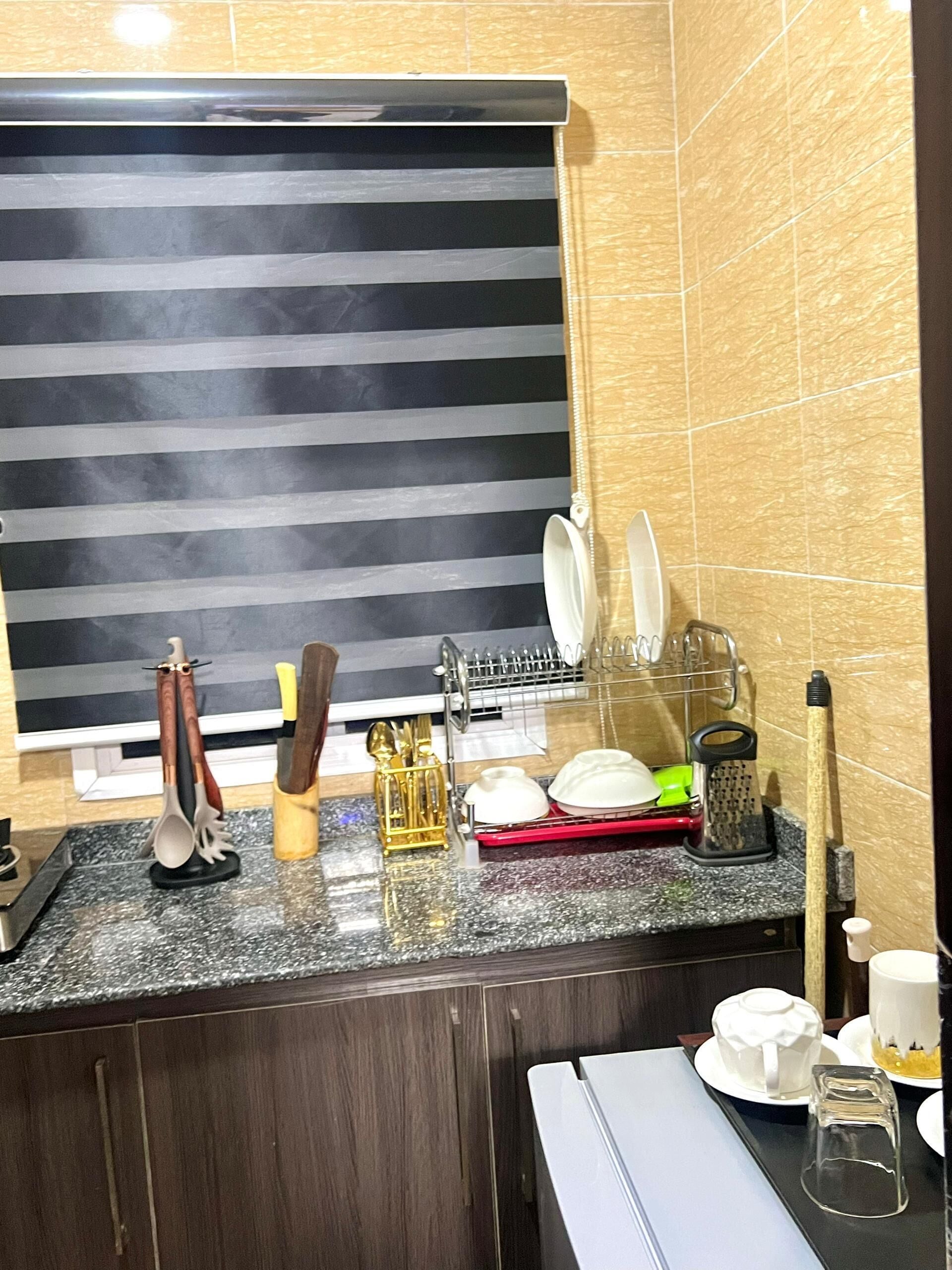 Una cocina con una persiana a rayas negras, encimera de granito y diferentes utensilios y electrodomésticos.