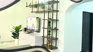 En moderne stue med en hvid sofa, et fjernsyn og en dekorativ reol med planter og en cykel.