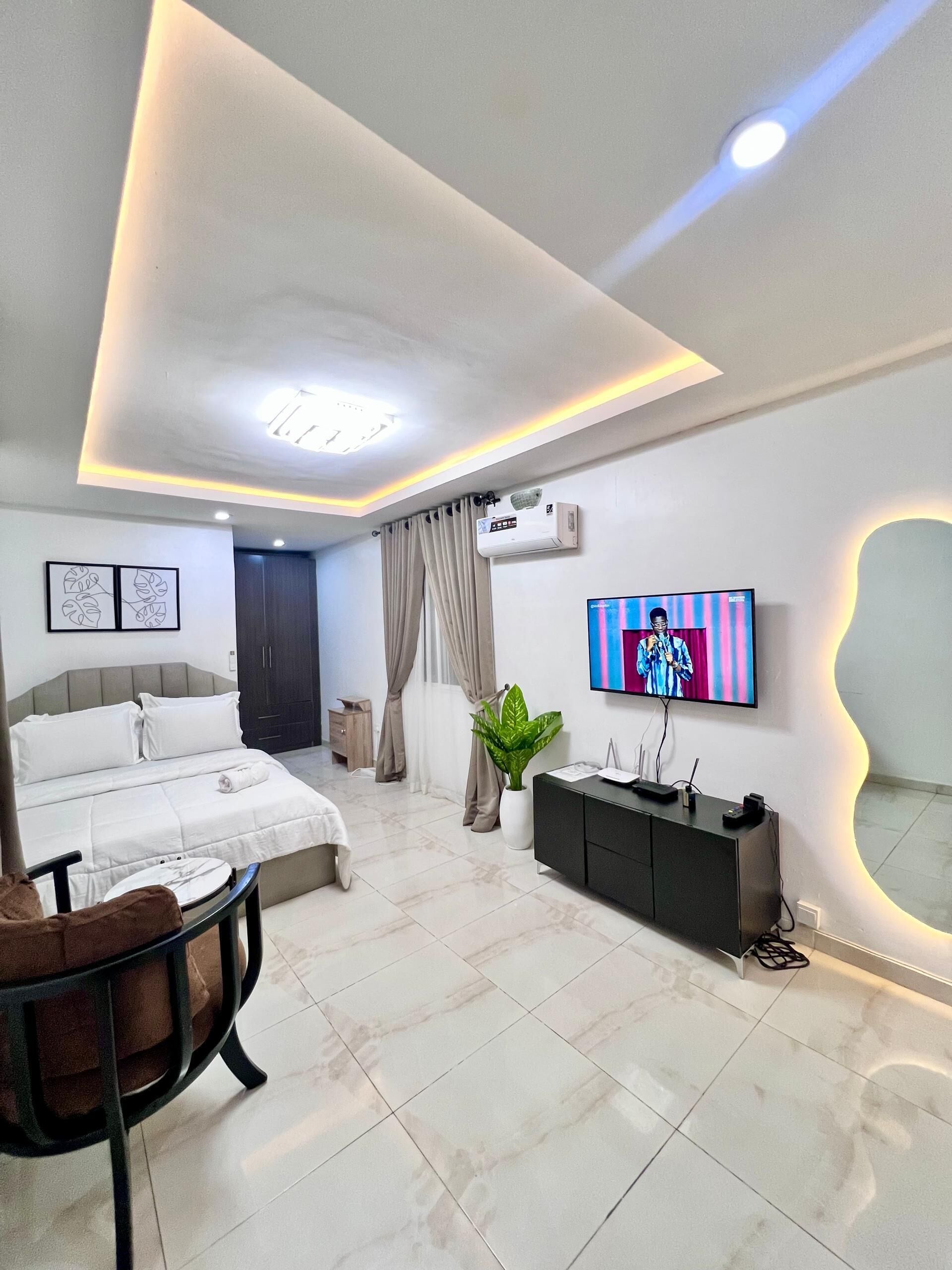 Ein modernes Hotelzimmer mit Bett, Fernseher, Schreibtisch, Stuhl und einer Zimmerpflanze.