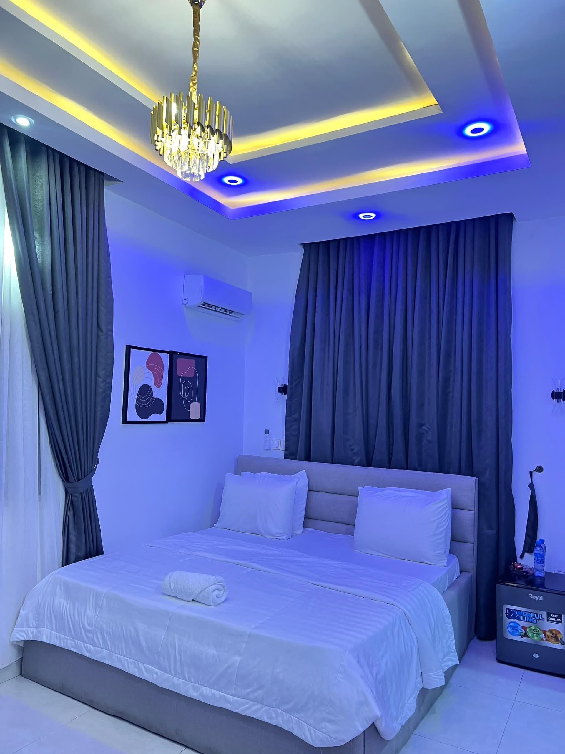 A modern bedroom with a bed, curtains, a chandelier, and a wall-mounted air conditioner.