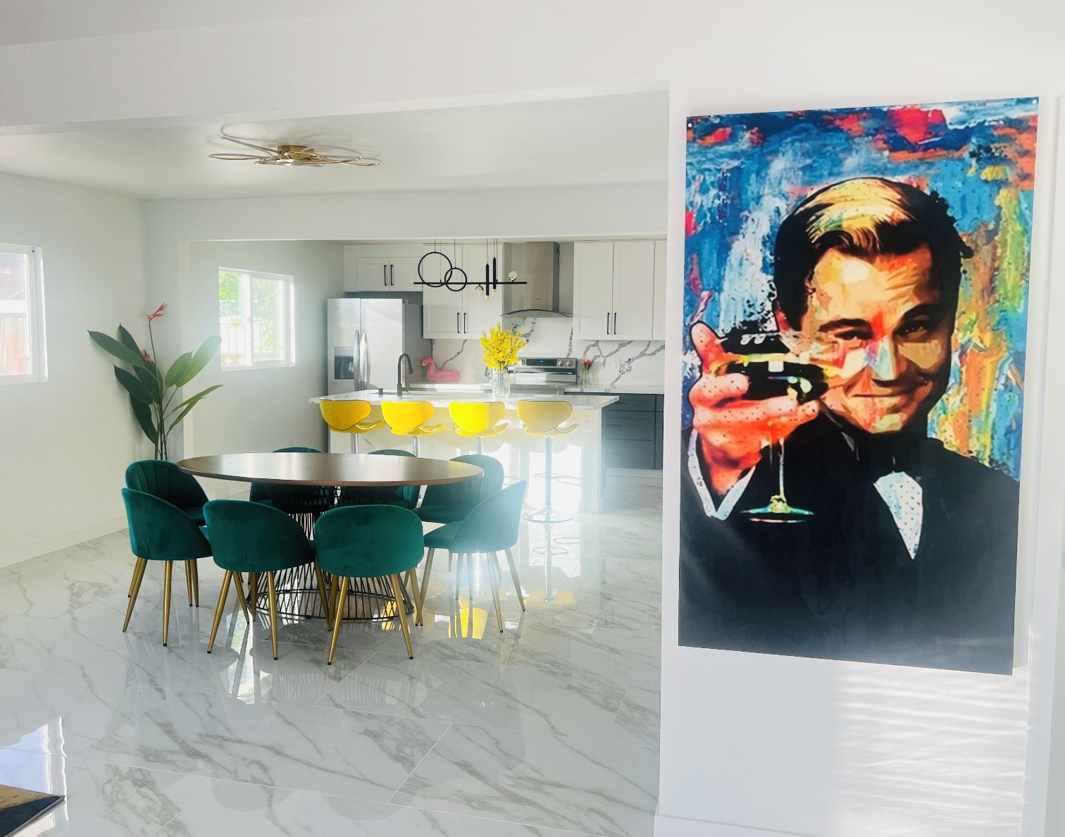 A modern kitchen with white cabinets, a central island with yellow chairs, and a dining area with a round table and teal chairs.