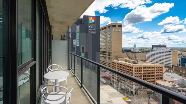 A balcony with two white tables and chairs, overlooking a cityscape with modern buildings and a clear sky.