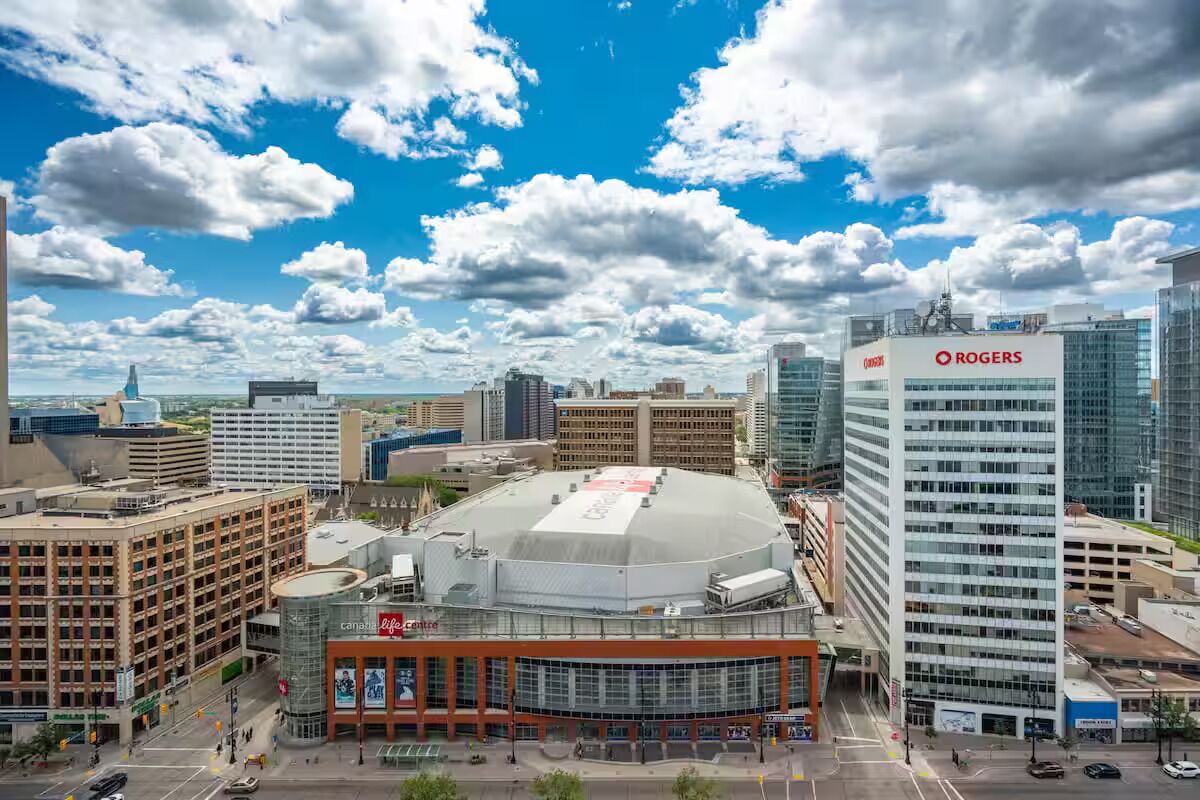 A cityscape with a prominent Rogers building, a large stadium, and surrounding modern architecture.