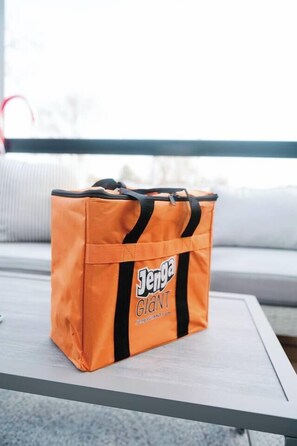 En orange väska med texten ”Jenya GIANI” på, placerad på ett vitt bord.