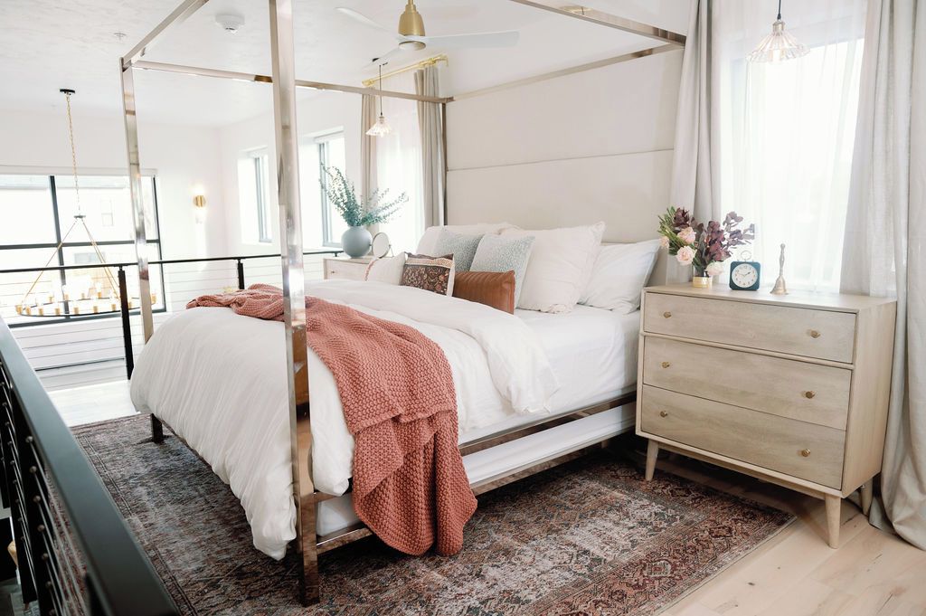 A four-poster bed with a canopy, a bedside table with a clock, and a view of a balcony.