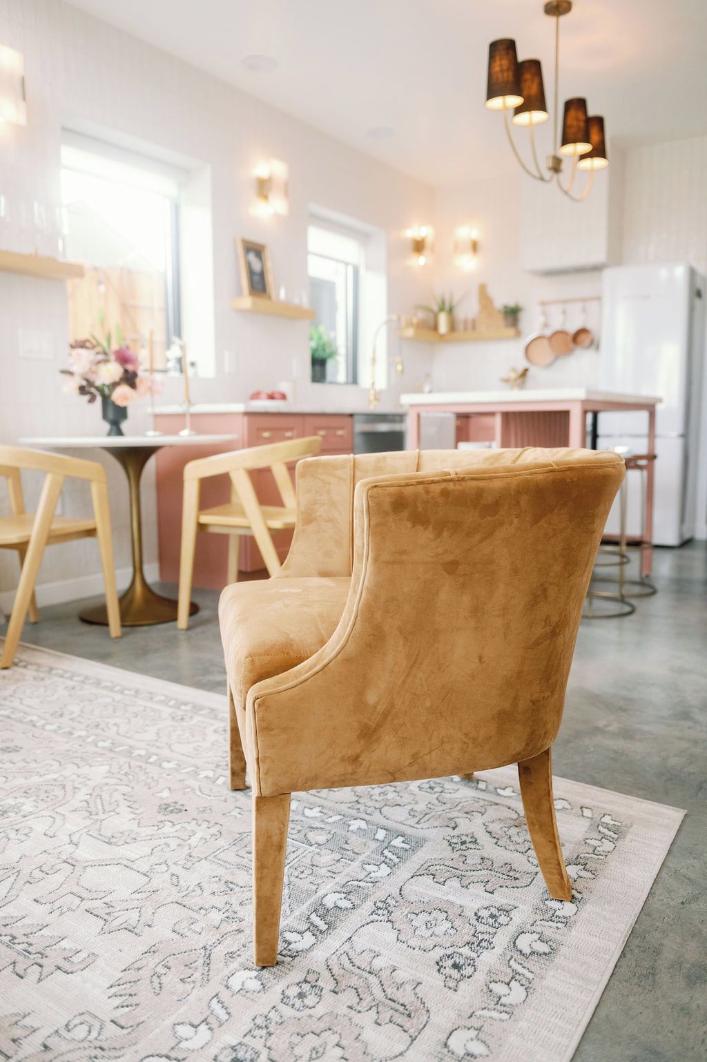 Une cuisine moderne avec un coin repas, comprenant un fauteuil en velours, un tapis à motifs et des luminaires suspendus.