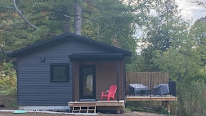 Une petite cabane avec un porche, une chaise rouge et un espace abrité avec une table.